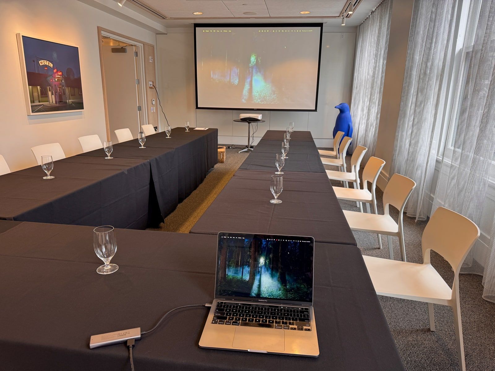A boutique hotel meeting room set up boardroom-style with a large screen mirroring a laptop presentation.